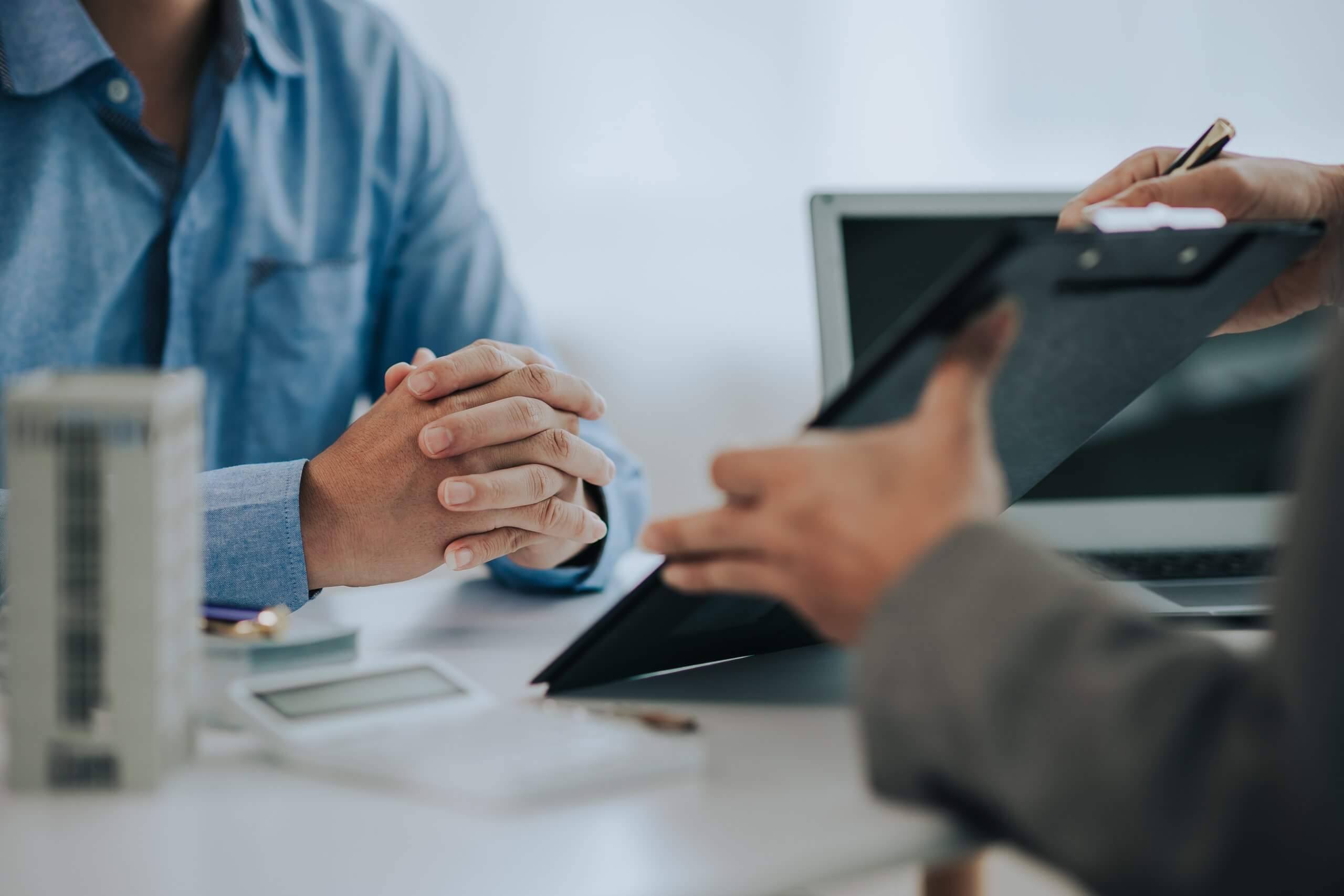 Close-up photo of a real estate agent offering a contract to purchase or rent a residence. Businessman holds small house model with property insurance at table in home sales office