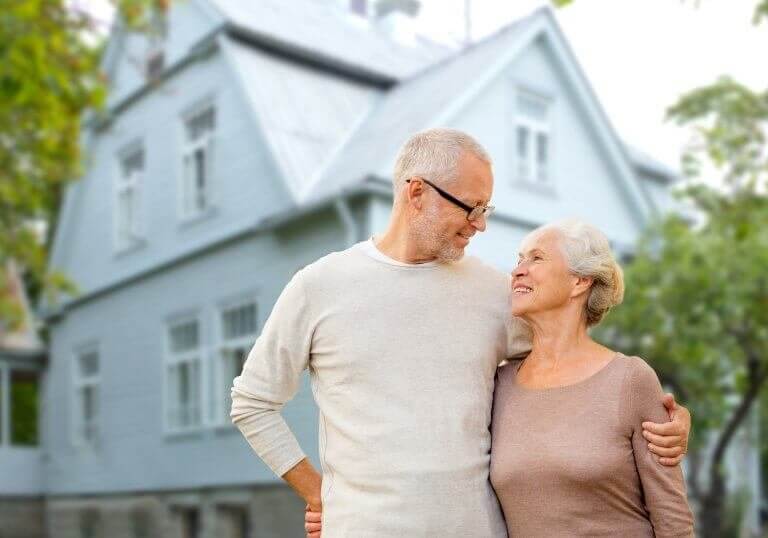 old age, accommodation and real estate concept - happy senior couple hugging over house background